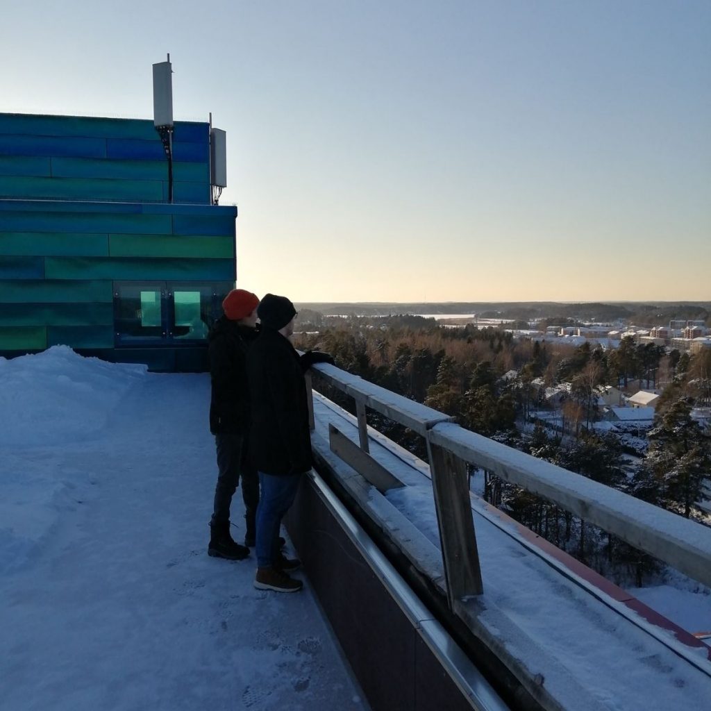 Kai ja Aleksi Aimaterin toimistorakennuksen Piispantornin kattoterassilla katsomassa lumista talvimaisemaa alkuvuodesta 2021. Taustalla näkyy Piispanristiä ja Katariinan laaksoa.
