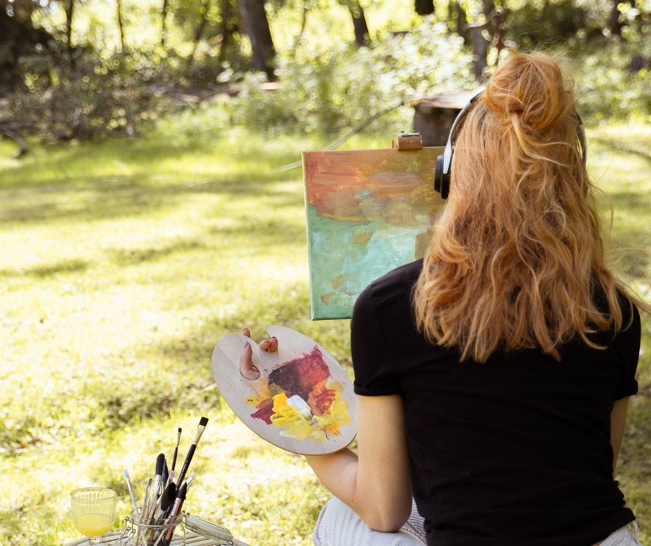 Nainen maalaa taulua kesällä ulkona kuulokkeet päässä.