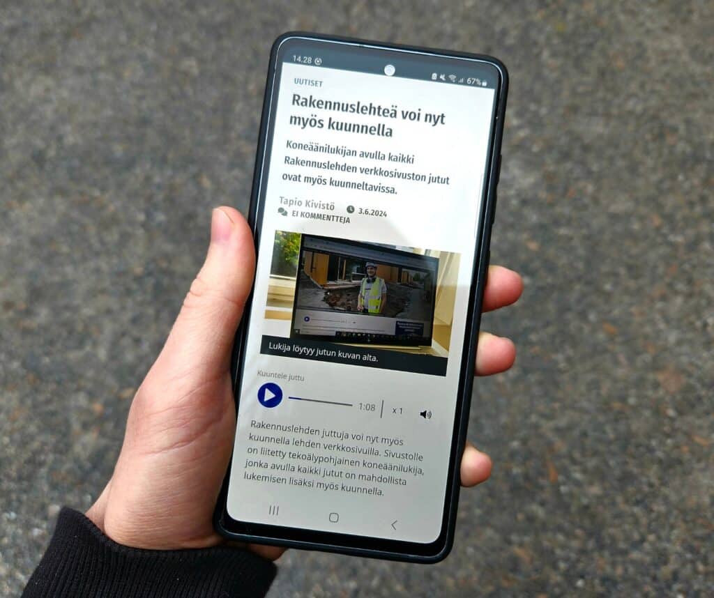 Kännykän näyttö, jossa näkyy Rakennuslehden artikkeli, joka kertoo, että Rakennuslehden artikkelit ovat nyt kuunneltavia. Kännykkää pitelee käsi ja taustalla näkyy sepeliä.